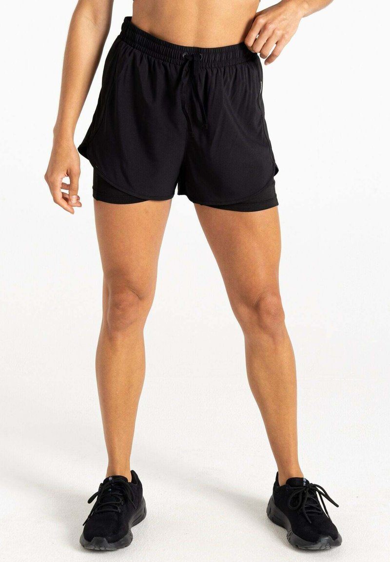 Pantalones cortos deportivos negros con un corte holgado y forro interior, con una cinturilla elástica y cordón de ajuste. Combinados con zapatillas deportivas negras.