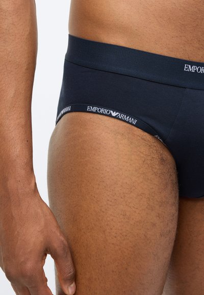 Navy zilas kokvilnas biksītes ar elastīgu jostasvietu un baltu "Emporio Armani" logotipu. Gluda tekstūra, pieguļošs dizains, minimāla pārklājuma zona.