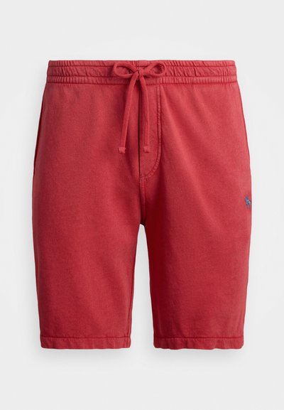 Røde shorts laget av et mykt stoff. Har et elastisk midjebånd med en snor og en subtil logo brodert i blått på siden.