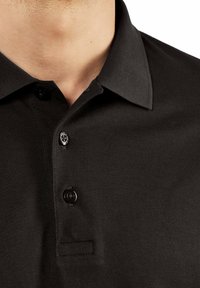 Czarny polo z teksturowanej tkaniny, z kołnierzykiem, trzema guzikami i listwą. Zbliżenie podkreśla detale i ściegi.