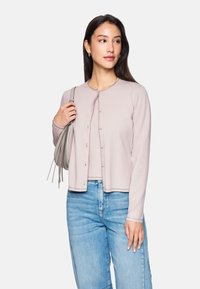 Hellrosa Strickjacke mit runder Halslinie, Knopfleiste und geripptem Saum; kombiniert mit hellblauen Jeans.