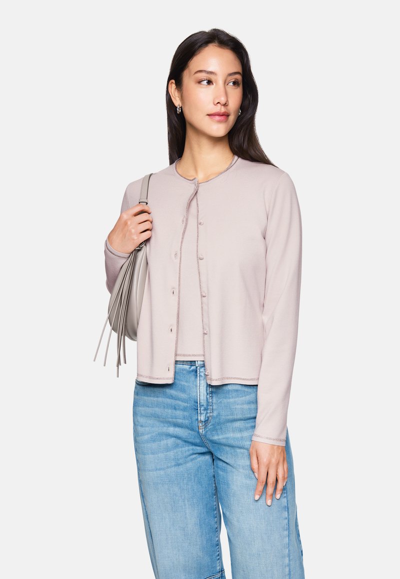 Hellrosa Strickjacke mit runder Halslinie, Knopfleiste und geripptem Saum; kombiniert mit hellblauen Jeans.