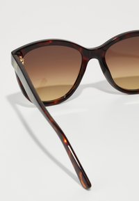 Óculos de sol estilo gato com padrão tartaruga, lentes castanhas em degradê e aros de plástico elegantes. Apresenta hastes finas com detalhes em dourado.