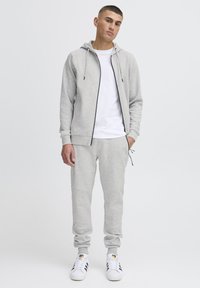 Gray hoodie and sweatpants set made from soft fabric. Hoodie features a zip, drawstrings, and front pockets. White t-shirt and sneakers included.