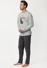 Camiseta de pijama de manga larga gris con un diseño gráfico; pantalones negros con un patrón multicolor de pequeños iconos y símbolos; ajuste casual.