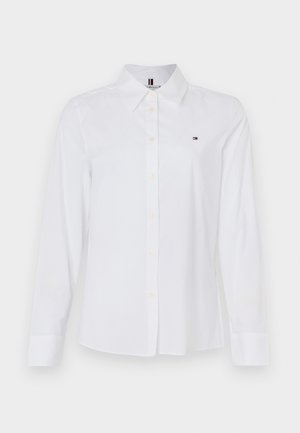 White long-sleeve button-up shirt made of cotton, featuring a classic collar, subtle logo on the chest, and yellow buttons.