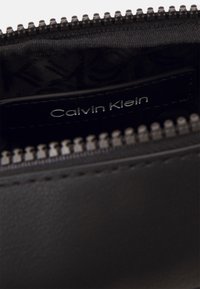 Pochette in pelle nera con chiusura a zip, dotata di etichetta interna con marchio e texture liscia. Denti della zip in metallo visibili.