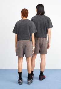 Grå mineralvaskede t-shirts parret med brune fløjlsbukser med store baglommer. Sorte knæhøje sokker og sneakers fuldender looket.