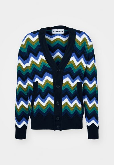 Dažādkrāsains adīts džemperis ar zigzaga rakstu jūras zilā, zaļā, baltā un zilā krāsā, ar V-veida kakla izgriezumu, pogām un kabatām.