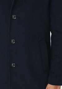 Granatowy wełniany płaszcz z podwójnym zapięciem, sześcioma czarnymi guzikami, kieszenią boczną oraz fakturowanym wykończeniem tkaniny.