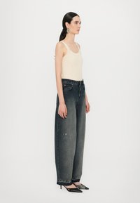 Top in maglia a costine crema abbinato a jeans oversized grigi scuri, con finitura sbiadita e orli risvoltati, completato da tacchi neri.