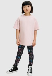 Rosa oversized t-shirt, svarta leggings med färgglatt sprutmönster och svarta högklackade sneakers med vita sulor. Enkel och avslappnad design.
