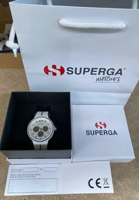 Reloj blanco con esfera redonda plateada, subesferas negras y correa negra. Presentado en una caja negra con papeles blancos y una bolsa de compras.