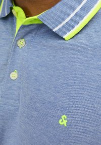 Light blue polo shirt with a textured fabric, featuring a neon green collar, white stripes, and matching buttons. Small green logo on the chest.