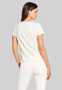 Witte katoenen t-shirt met korte mouwen, ronde halslijn en zijnaaddetails; weergegeven vanuit de achterkant tegen een grijze achtergrond.