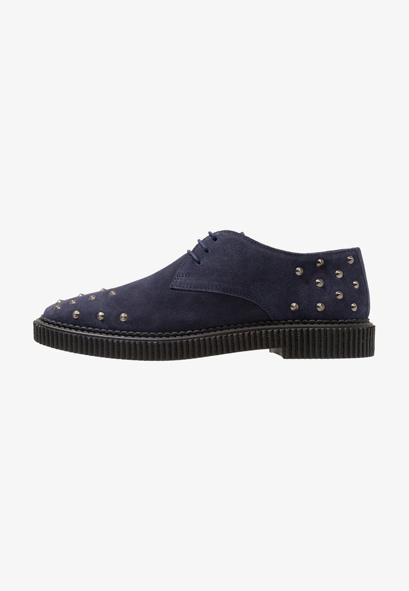 Chaussure habillée en daim bleu marine avec bout rond, semelle en caoutchouc et clous métalliques disposés de manière décorative sur la tige. Design à cinq œillets.