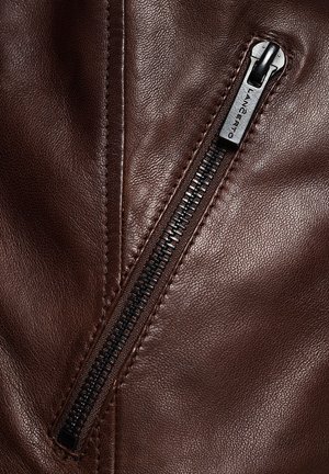 Brązowa skórzana kurtka z widocznym czarnym zamkiem błyskawicznym i szwami. Skóra ma gładką teksturę z subtelnymi detalami ziarna.