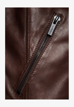 Brązowa skórzana kurtka z widocznym czarnym zamkiem błyskawicznym i szwami. Skóra ma gładką teksturę z subtelnymi detalami ziarna.