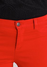 Røde denimjeans med en glat tekstur, der har lukning med knapper foran og et klassisk design med fem lommer samt synlige syningsdetaljer.