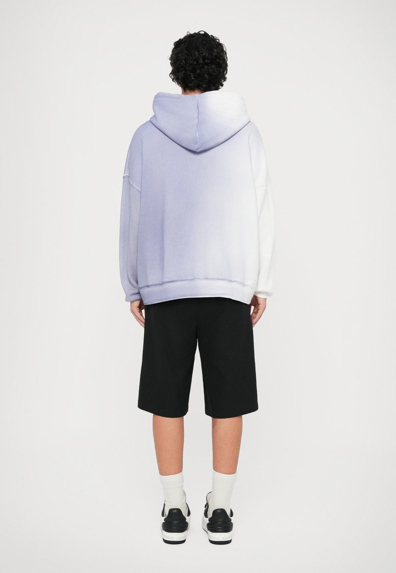 Lilla-til-hvid gradient oversized hoodie med hætte, parret med sorte shorts. Glat stof, ribbede manchetter og kant. Sort og hvid sneakers.