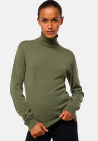 Pull à col roulé vert olive en texture tricot douce. Doté de manches longues et d'une silhouette ajustée avec des poignets et un ourlet côtelés.