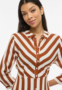 Robe chemise rayée marron et blanc avec un col à revers, une ouverture boutonnée à l'avant et des manches longues. Tissu lisse avec des rayures diagonales.