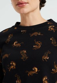 Närbild av en person som bär en svart skjorta med små, orange och bruna tiger mönster i olika poser över tyget.