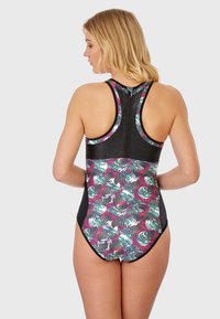 Le maillot de bain dos nageur présente une base noire avec un motif de feuilles tropicales colorées en vert, rose et gris. Texture lisse, détail zippé au dos.