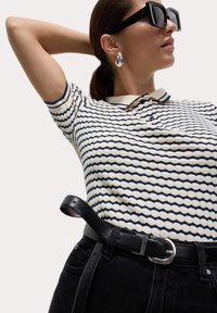 Gebreid polo shirt met marineblauwe golfstrepen, witte kraag, gecombineerd met hoge zwarte spijkerbroek en een zwarte leren riem met een zilveren gesp.