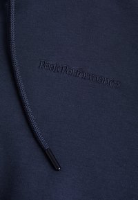 Mörkblå hoodie i texturerat tyg, med en framträdande broderad "Peak Performance" logotyp och en dragsko med svarta metalldelar.