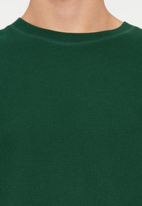 Groene, getextureerde katoenen sweater met een ronde hals en geribbelde manchetten, voorzien van een fijn wafelbreipatroon op het oppervlak van de stof.