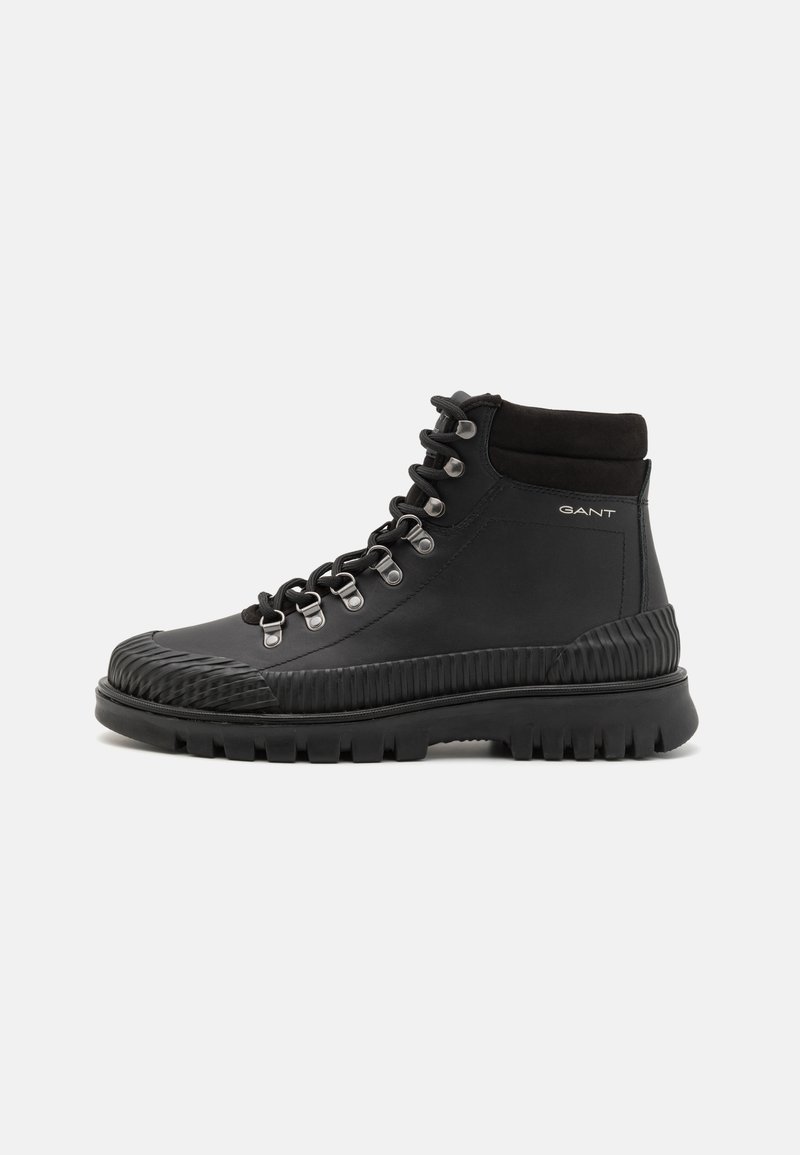 Czarne buty trekkingowe z gładką skórzaną cholewką, gumowym akcentem na palcach, metalowymi oczkami i wytrzymałą, teksturowaną podeszwą. Logo marki po boku.