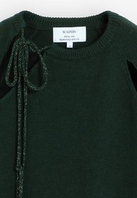 Zelený pletený svetr s kulatým výstřihem a bočními zavazovacími detaily s metalickým leskem. Štítek nese nápis "SCALPERS, SPECIAL YARN, S."