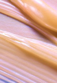 Kremowy produkt kosmetyczny o gładkiej, błyszczącej teksturze w odcieniach brzoskwini i lawendy, z subtelnymi akcentami połysku.