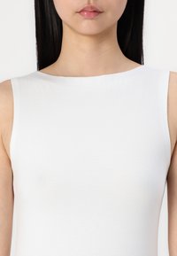 Weißes ärmelloses Top mit hohem Ausschnitt, glatter Textur und figurnahem Schnitt, entworfen für eine minimalistische Ästhetik.