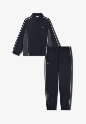 Granatowy dres składa się z kurtki na zamek z białymi lamówkami oraz pasujących spodni. Wykonany z gładkiego materiału, zawiera detal z logo Lacoste.