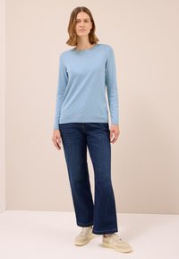 Helles blauer Pullover mit langen Ärmeln, Rundhalsausschnitt, kombiniert mit dunkelblauen, weit geschnittenen Jeans und beigen Sneakers. Glatte Stoffstruktur, lässige Passform.