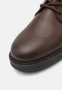 Brune lærskof med en glat, struktureret finish. Rund tå og mørk gummisål med synlige dækmønstre. Snørebåndene er brune og flade.