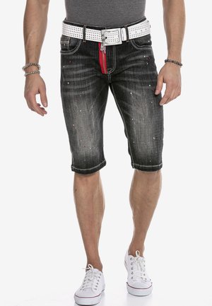 Schwarze Denim-Shorts mit einem ausgewaschenen Finish, rotem Reißverschluss, weißem Nieten-Gürtel und Spritzdetails. Mit umgeschlagenen Säumen und typischem Fünf-Taschen-Design.