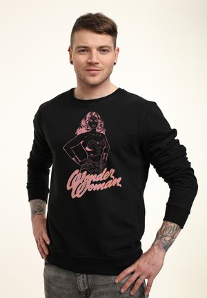 Schwarzes Sweatshirt mit einer pinken Grafik von Wonder Woman und dem Text "Wonder Woman". Das Design umfasst lange Ärmel und einen runden Halsausschnitt.