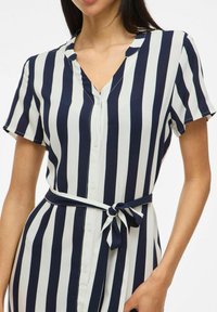 Abito a righe verticali blu navy e bianche realizzato in tessuto leggero, con apertura frontale a bottoni, maniche corte e cintura con nodo in vita.