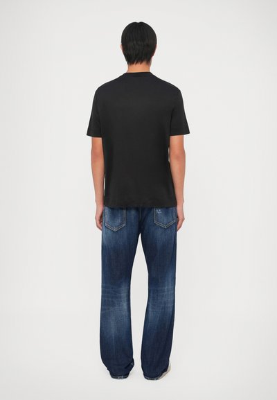 T-shirt preta de manga curta combinada com jeans de denim azul de corte largo. Os jeans apresentam um design clássico de cinco bolsos com desbotamento subtil.