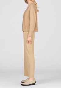 Beżowy sweter dzianinowy o luźnym kroju, zestawiony z beżowymi spodniami o szerokich nogawkach oraz jasnymi mokasynami. Prosty design o gładkiej fakturze.