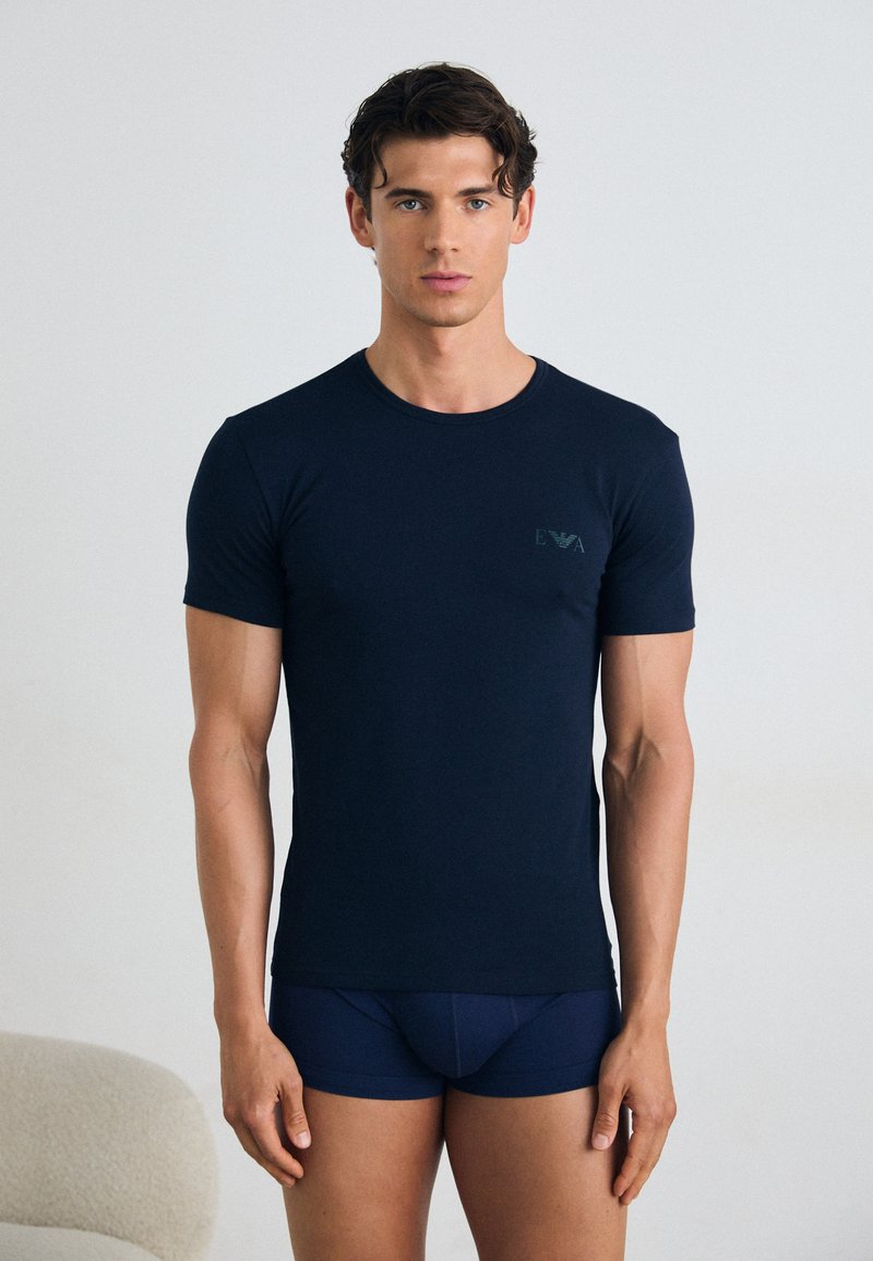 T-shirt bleu marine à manches courtes en tissu doux, avec un col rond et un logo discret sur la poitrine gauche.