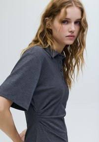 Szürke rövid ujjú poló, gombos gallérral és finom textúrával. Testhez simuló kialakítás oldalsó varratokkal a szabott megjelenésért.
