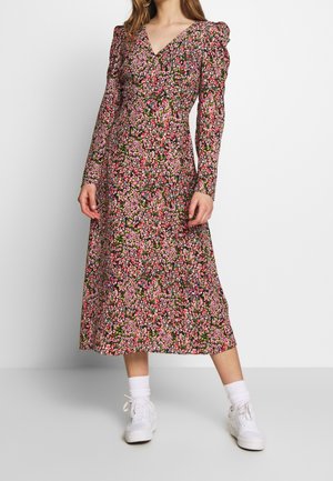 Robe à manches longues florale en noir avec des motifs roses et verts. Dotée d'un décolleté en V et de manches bouffantes froncées, associée à des baskets blanches.