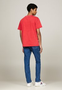 Camiseta de algodón roja con un corte holgado, cuello redondeado y mangas cortas, combinada con jeans de mezclilla azul y zapatillas blancas.