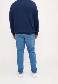 Blå tröja med rund halsringning och ribbade manschetter, i kombination med ljusblå denimjeans. Jeansen har klassiska bakfickor och en avslappnad passform.