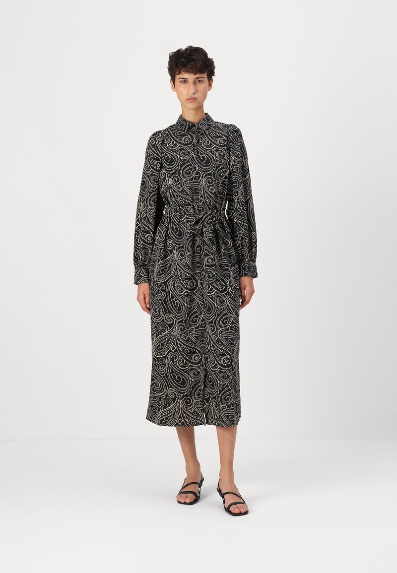 Robe noire à manches longues avec un motif paisley en crème. Présente un col et une ceinture à nouer à la taille. Texture lisse.