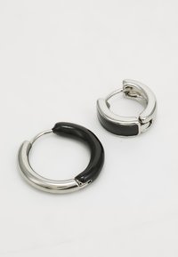 Orecchini a cerchio neri e argento caratterizzati da una fascia nera lucida e accenti in metallo argento brillante, con un design curvo e aperto.